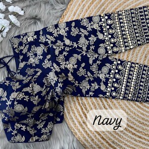 May include: A navy blue blouse featuring a gold floral pattern and long sleeves with horizontal bands of gold embroidery and sequins. The garment includes a tie-back closure with tassels and is labeled with the word navy in the bottom corner.