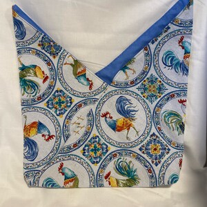 May include: A fabric tote bag with a rooster pattern. The bag features a white background with circular designs in blue, yellow, and green, each containing a rooster illustration. The top edge is lined with a solid blue fabric.