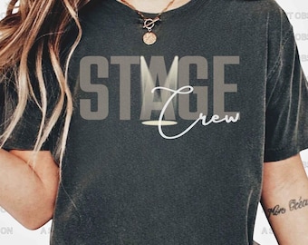 May include: A dark gray t-shirt with the text "STAGE Crew" in white and black lettering. The "A" in "STAGE" is replaced with a spotlight graphic.