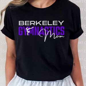 Puede incluir: Camiseta negra con el texto "BERKELEY GYMNASTICS Mom" en blanco y morado. Se incluye una silueta de una gimnasta en el texto.