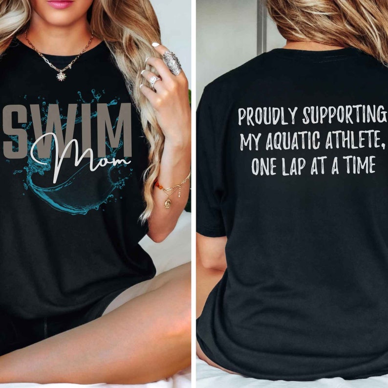 Może przedstawiać: Czarny T-shirt z napisem "Swim Mom" w kolorze szarym i niebieskim wzorem rozbryzgującej się wody z przodu. Z tyłu T-shirtu znajduje się napis "Proudly supporting my aquatic athlete, one lap at a time" w kolorze białym.