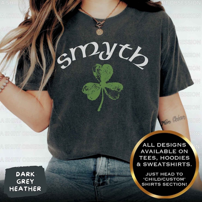 May include: A dark heather grey t-shirt with the word "smyth" in white lettering and a green shamrock graphic. The text "ALL DESIGNS AVAILABLE ON TEES, HOODIES & SWEATSHIRTS. JUST HEAD TO 'CHILD/CUSTOM' SHIRTS SECTION!" is printed on the bottom right corner of the shirt.