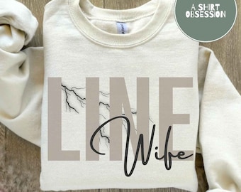 May include: A cream-colored sweatshirt with the text "LINE Wife" in black and brown lettering. A lightning bolt graphic is incorporated into the design.