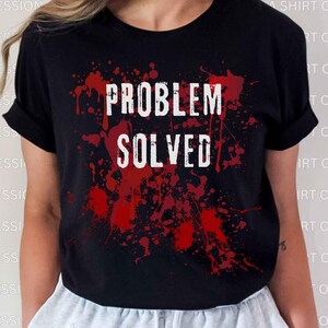 Peut inclure: T-shirt noir avec l'inscription blanche « PROBLEM SOLVED ». Le texte est superposé à un motif éclaboussé rouge. Le t-shirt a des manches courtes et un col rond.