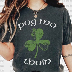 May include: A dark gray t-shirt with a white shamrock and the text "pog mo thoin" in white.