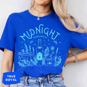 May include: A blue t-shirt featuring a white graphic design of a bottle of tequila, a margarita glass, and a mortar and pestle. The text "MIDNIGHT MARGARITAS" is written in a whimsical font above the design.