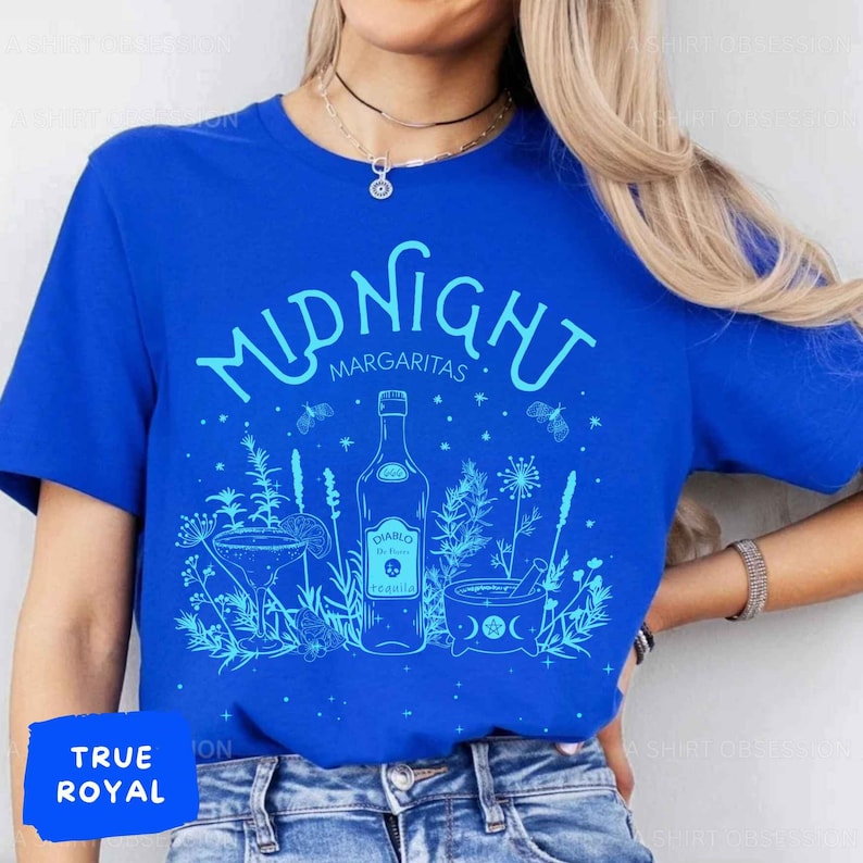 May include: A blue t-shirt featuring a white graphic design of a bottle of tequila, a margarita glass, and a mortar and pestle. The text "MIDNIGHT MARGARITAS" is written in a whimsical font above the design.