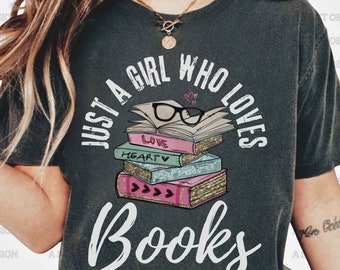 May include: A dark gray t-shirt with a white graphic design that says "Just a girl who loves books". The graphic features a stack of books with a pair of glasses on top, and the words "Love" and "Heart" are visible on the books.