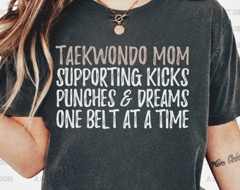 Peut inclure: Un t-shirt gris avec le texte "Taekwondo Mom Supporting Kicks Punches & Dreams One Belt At A Time" en blanc.