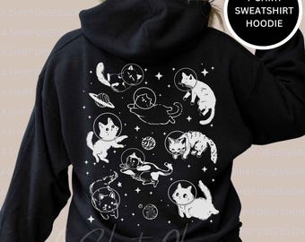 May include: Black hoodie with a white print of cats wearing astronaut helmets and floating in space. The text "T-SHIRT SWEATSHIRT HOODIE" is in a white box in the upper right corner of the image.