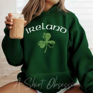 May include: Green hooded sweatshirt with a white graphic of a shamrock and the word "ireland" in a stylized font.