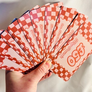 Puede incluir: Un abanico de tarjetas a cuadros rojos y blancos. Cada tarjeta tiene el texto "Fifty Pounds" en una fuente lúdica, con un borde ondulado.