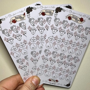 Può includere: Tre fogli di carta adesiva bianca con illustrazioni in nero e rosso di diversi piercing per il corpo. Gli adesivi sono etichettati "Piercing Fund".