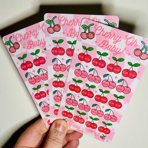 Puede incluir: Cuatro tarjetas rosas y blancas con un patrón a cuadros y cerezas. Las tarjetas tienen el texto "Cherry Baby" y "Cherry Oh Baby!" y un total de 100 £.