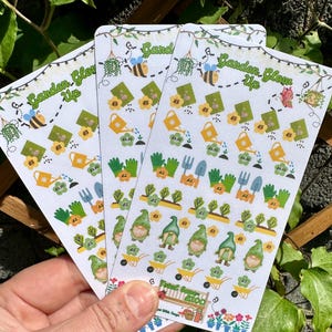 Op de afbeelding: Drie vellen stickers met een tuinthema. De stickers bevatten gnomen, gieters, bloemen en andere tuin gerelateerde items. De stickers zijn gelabeld "Garden Glow Up" en hebben prijzen in pond sterling.
