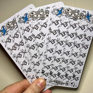 May include: Four white sheets of sticker paper with a black and white tattoo themed design. The design includes a tattoo machine, a crown, a lightning bolt, a chain, and a diamond. The text "Tattoo Fund" is printed on the top of each sheet.