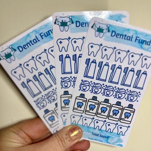 May include: Four sheets of stickers with a blue and white watercolour background. The stickers feature various dental-themed illustrations, including teeth, toothbrushes, toothpaste, and mouthwash. The text "Dental Fund" and "Total Saved" is printed on the stickers.