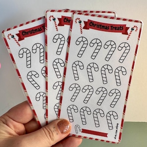 Könnte beinhalten: Drei Blätter mit weihnachtlichen Aufklebern mit Zuckerstangen-Designs. Die Aufkleber sind weiß mit schwarzen Umrissen und auf durchsichtigen Blättern gedruckt. Der Text "Christmas Treats" ist auf dem oberen Blatt gedruckt.