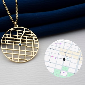 May include: Gold pendant necklace with a circular, openwork city map design. A small, dark blue gemstone is set in the centre. The necklace hangs on a gold chain.