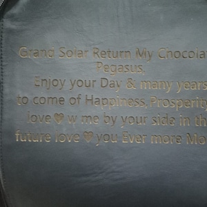K&ouml;nnte beinhalten: Ein schwarzer Lederrucksack mit einer goldenen Inschrift, die lautet: "Grand Solar Return My Chocolate Pegasus, Enjoy your Day & many years to come of Happiness, Prosperity & love w me by your side in the future love you Ever more Monet".