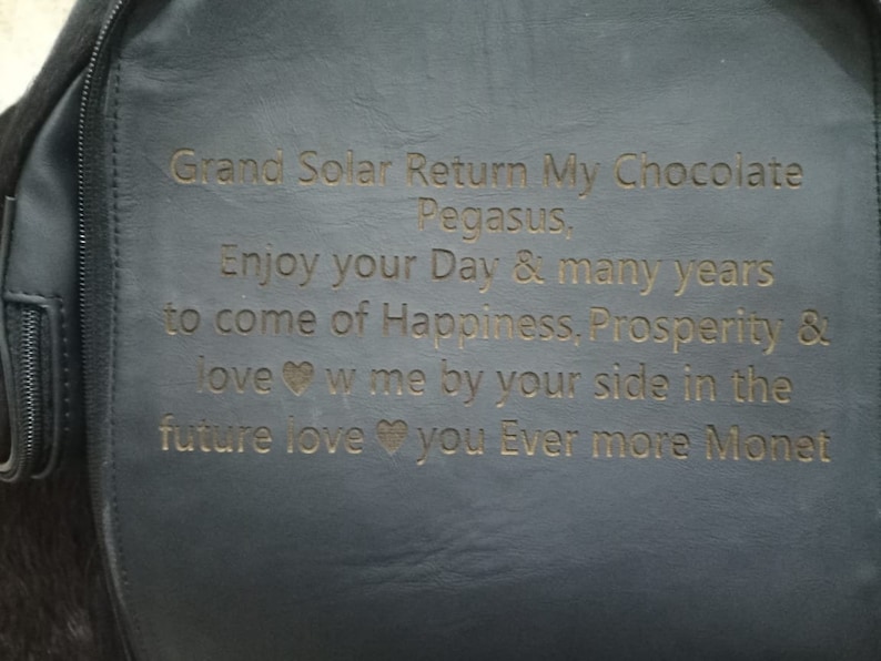 K&ouml;nnte beinhalten: Ein schwarzer Lederrucksack mit einer goldenen Inschrift, die lautet: "Grand Solar Return My Chocolate Pegasus, Enjoy your Day & many years to come of Happiness, Prosperity & love w me by your side in the future love you Ever more Monet".