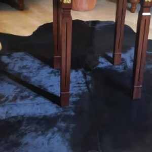 Pu&ograve; includere: Un tappeto in pelle di mucca blu scuro con due gambe di legno di un tavolo sopra.