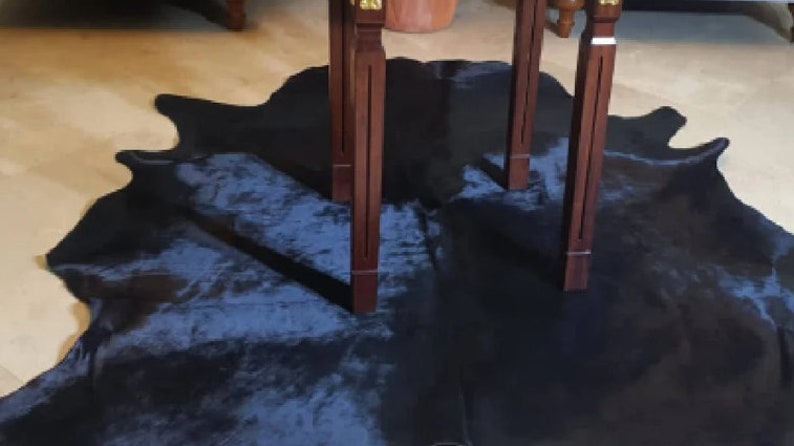 Pu&ograve; includere: Un tappeto in pelle di mucca blu scuro con due gambe di legno di un tavolo sopra.