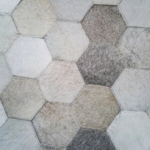 Pu&ograve; includere: Un tappeto in pelle di mucca bianco e grigio con un motivo esagonale. Il tappeto &egrave; composto da pezzi singoli di pelle di mucca cuciti insieme.