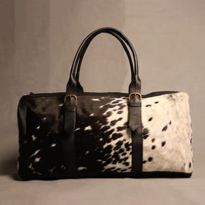 Personalized Large Cowhide Duffel Bag made from genuine hair-on leather. This unisex, handmade travel bag is perfect for weekend getaways or daily use. Spacious and stylish with multiple compartments, it offers both function and flair. The adjustable strap adds comfort, while real cowhide ensures each bag is unique. A thoughtful gift for him or her. Note: Natural cowhide patterns vary, making every piece one-of-a-kind.