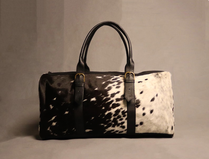 Personalized Large Cowhide Duffel Bag made from genuine hair-on leather. This unisex, handmade travel bag is perfect for weekend getaways or daily use. Spacious and stylish with multiple compartments, it offers both function and flair. The adjustable strap adds comfort, while real cowhide ensures each bag is unique. A thoughtful gift for him or her. Note: Natural cowhide patterns vary, making every piece one-of-a-kind.