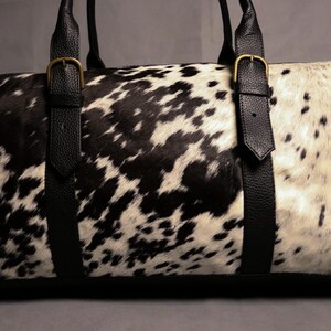Personalized Large Cowhide Duffel Bag made from genuine hair-on leather. This unisex, handmade travel bag is perfect for weekend getaways or daily use. Spacious and stylish with multiple compartments, it offers both function and flair. The adjustable strap adds comfort, while real cowhide ensures each bag is unique. A thoughtful gift for him or her. Note: Natural cowhide patterns vary, making every piece one-of-a-kind.