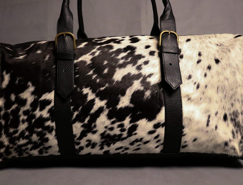 Personalized Large Cowhide Duffel Bag made from genuine hair-on leather. This unisex, handmade travel bag is perfect for weekend getaways or daily use. Spacious and stylish with multiple compartments, it offers both function and flair. The adjustable strap adds comfort, while real cowhide ensures each bag is unique. A thoughtful gift for him or her. Note: Natural cowhide patterns vary, making every piece one-of-a-kind.