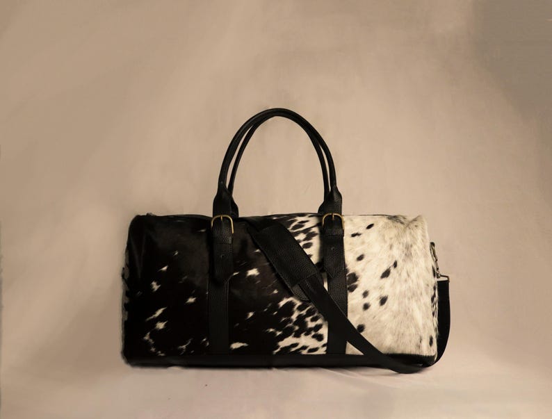 Personalized Large Cowhide Duffel Bag made from genuine hair-on leather. This unisex, handmade travel bag is perfect for weekend getaways or daily use. Spacious and stylish with multiple compartments, it offers both function and flair. The adjustable strap adds comfort, while real cowhide ensures each bag is unique. A thoughtful gift for him or her. Note: Natural cowhide patterns vary, making every piece one-of-a-kind.