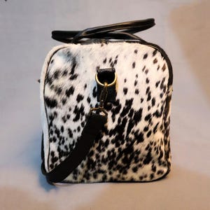 Personalized Large Cowhide Duffel Bag made from genuine hair-on leather. This unisex, handmade travel bag is perfect for weekend getaways or daily use. Spacious and stylish with multiple compartments, it offers both function and flair. The adjustable strap adds comfort, while real cowhide ensures each bag is unique. A thoughtful gift for him or her. Note: Natural cowhide patterns vary, making every piece one-of-a-kind.