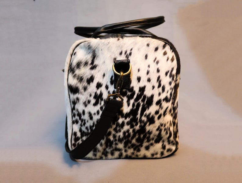 Personalized Large Cowhide Duffel Bag made from genuine hair-on leather. This unisex, handmade travel bag is perfect for weekend getaways or daily use. Spacious and stylish with multiple compartments, it offers both function and flair. The adjustable strap adds comfort, while real cowhide ensures each bag is unique. A thoughtful gift for him or her. Note: Natural cowhide patterns vary, making every piece one-of-a-kind.