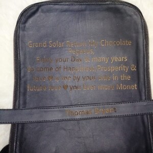 K&ouml;nnte beinhalten: Ein schwarzer Lederrucksack mit einer goldenen Inschrift, die lautet: "Grand Solar Return My Chocolate Pegasus, Enjoy your Day & many years to come of Happiness, Prosperity & love w me by your side in the future love you Ever more Monet" und "Thomas Bryant".