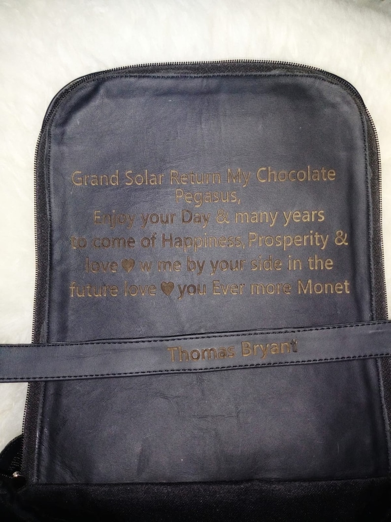 K&ouml;nnte beinhalten: Ein schwarzer Lederrucksack mit einer goldenen Inschrift, die lautet: "Grand Solar Return My Chocolate Pegasus, Enjoy your Day & many years to come of Happiness, Prosperity & love w me by your side in the future love you Ever more Monet" und "Thomas Bryant".
