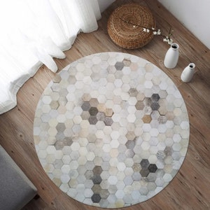 Pu&ograve; includere: Un tappeto rotondo in pelle di mucca, bianco e grigio, con un motivo esagonale. Il tappeto &egrave; composto da molti piccoli pezzi di pelle cuciti insieme.