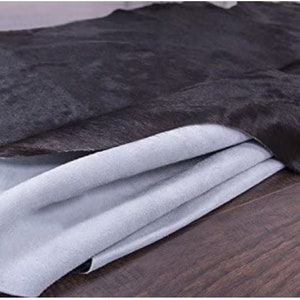 Pu&ograve; includere: Un tappeto in pelle di mucca nera con un retro bianco morbido. Il tappeto &egrave; piegato a met&agrave;, mostrando il retro bianco.