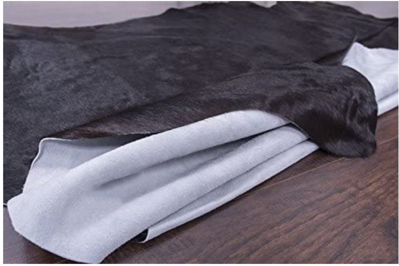 Pu&ograve; includere: Un tappeto in pelle di mucca nera con un retro bianco morbido. Il tappeto &egrave; piegato a met&agrave;, mostrando il retro bianco.