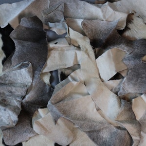 May include: A pile of gray and white cowhide leather scraps. The leather is soft and supple, with a natural grain pattern. The scraps are perfect for crafting projects, such as leatherworking, jewelry making, and home decor.