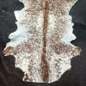 May include: A white cowhide rug with brown spots. The hide has been tanned and is soft and supple. It is a beautiful and unique piece of decor.