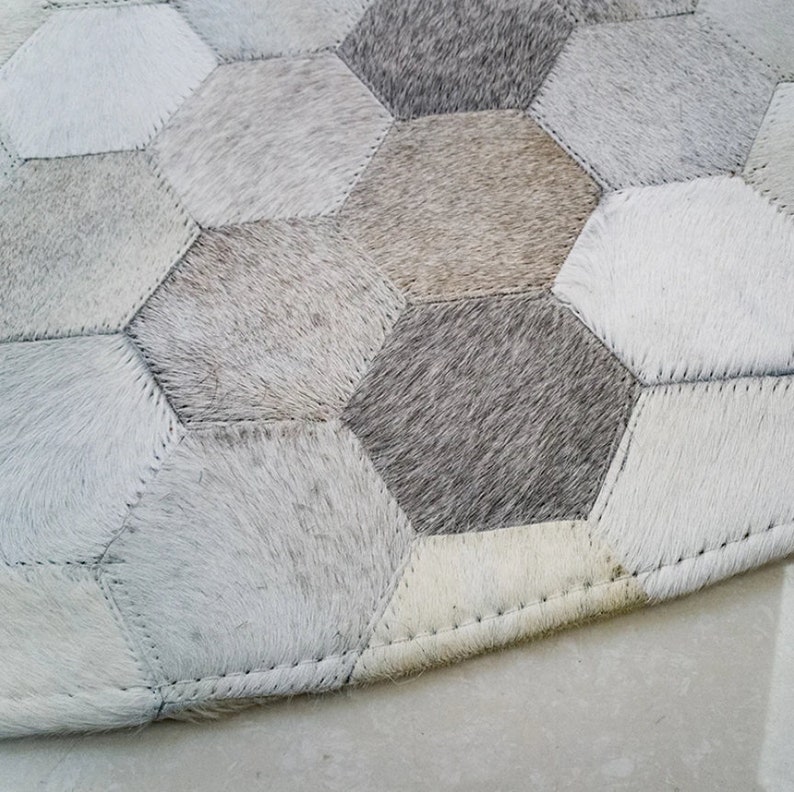 Pu&ograve; includere: Primo piano di un tappeto in pelle di mucca bianco e grigio con un motivo esagonale. Il tappeto &egrave; composto da pezzi singoli di pelle di mucca cuciti insieme.