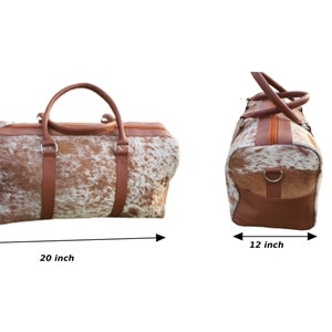 K&ouml;nnte beinhalten: Eine braune und wei&szlig;e Reisetasche aus Kuhfell mit braunen Lederverzierungen. Die Tasche ist 50,8 cm breit, 30,5 cm hoch und 25,4 cm tief.
