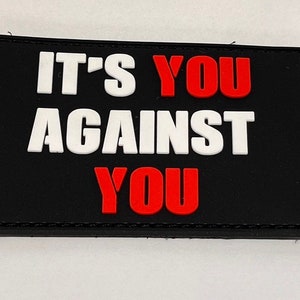 May include: Black patch with white and red text that reads "It's You Against You".