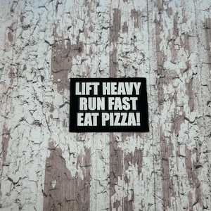 May include: Black and white sign with the text "Lift Heavy Run Fast Eat Pizza!" on a white textured background.