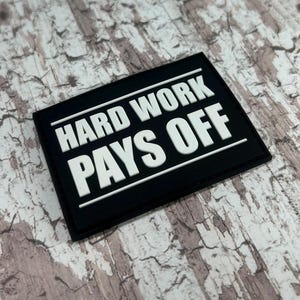 May include: Black and white patch with the text "Hard Work Pays Off" in white letters on a black background.