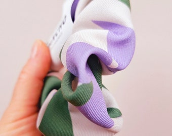 May include: A white, green, and purple patterned scrunchie. The scrunchie is made of fabric and has a gathered design.