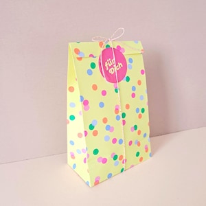 Könnte beinhalten: Eine gelbe Papiertüte mit bunten Konfetti-Punkten. Ein pinkfarbener Aufkleber mit der Aufschrift "für Dich" ist mit einer Schnur befestigt. Die Tüte ist oben verschlossen.