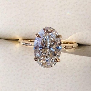 Puede incluir: Un anillo de compromiso de oro con un diamante de talla ovalada. El diamante, con sus m&uacute;ltiples facetas, es el punto focal. La banda es de oro pulido simple. El anillo se presenta sobre un fondo blanco.